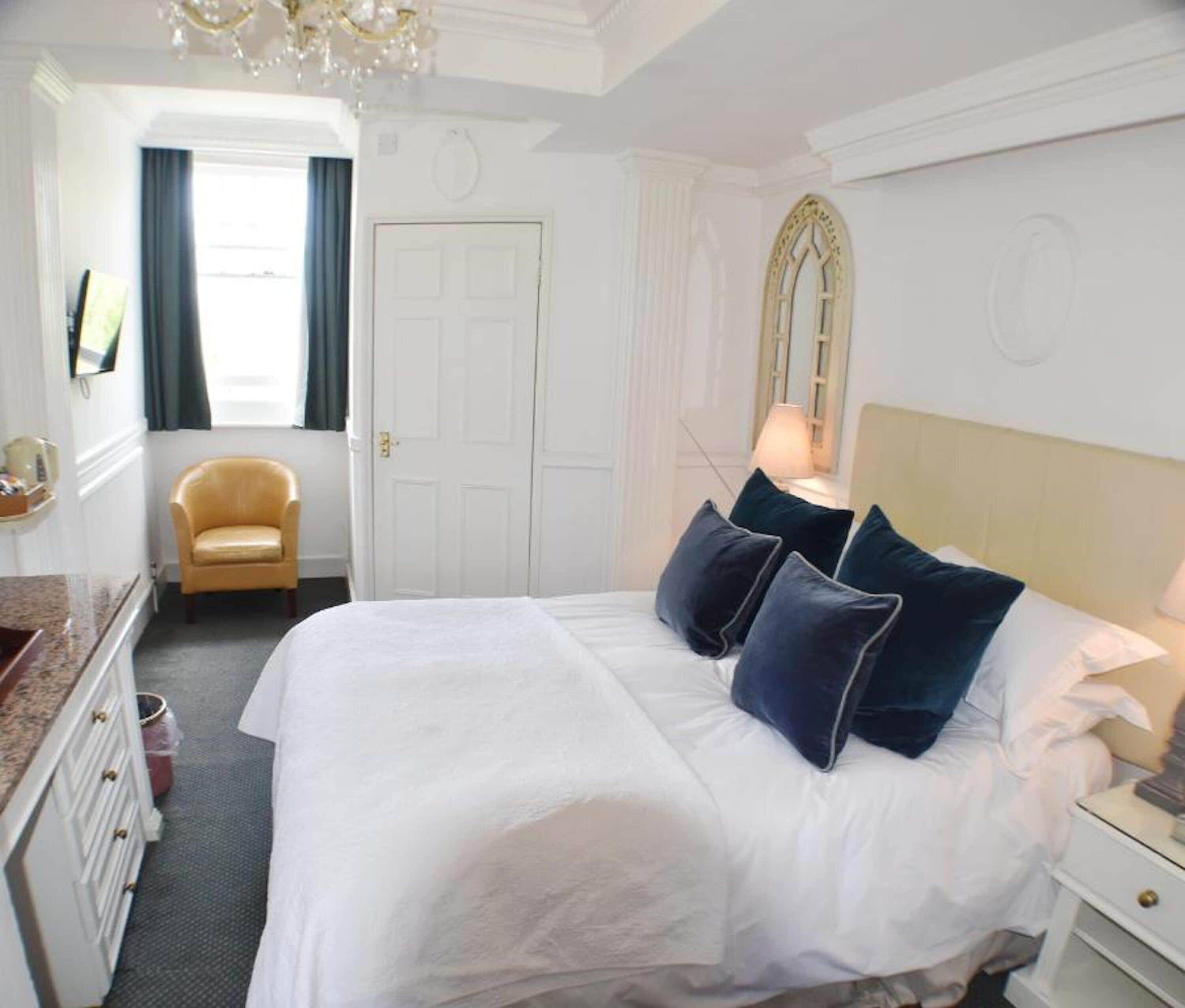 A hotel room with a large bed, a chair, a dresser, and a mirror on the wall.