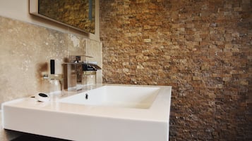 Un baño con un lavabo blanco, un espejo y una pared de ladrillo.