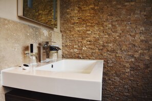 A bathroom with a white sink, a mirror, and a brick wall.