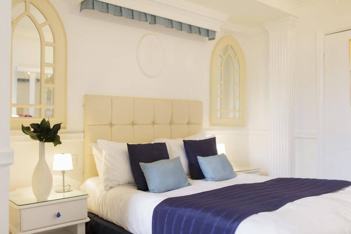 A hotel room with a large bed, a nightstand with a lamp, and a mirror.