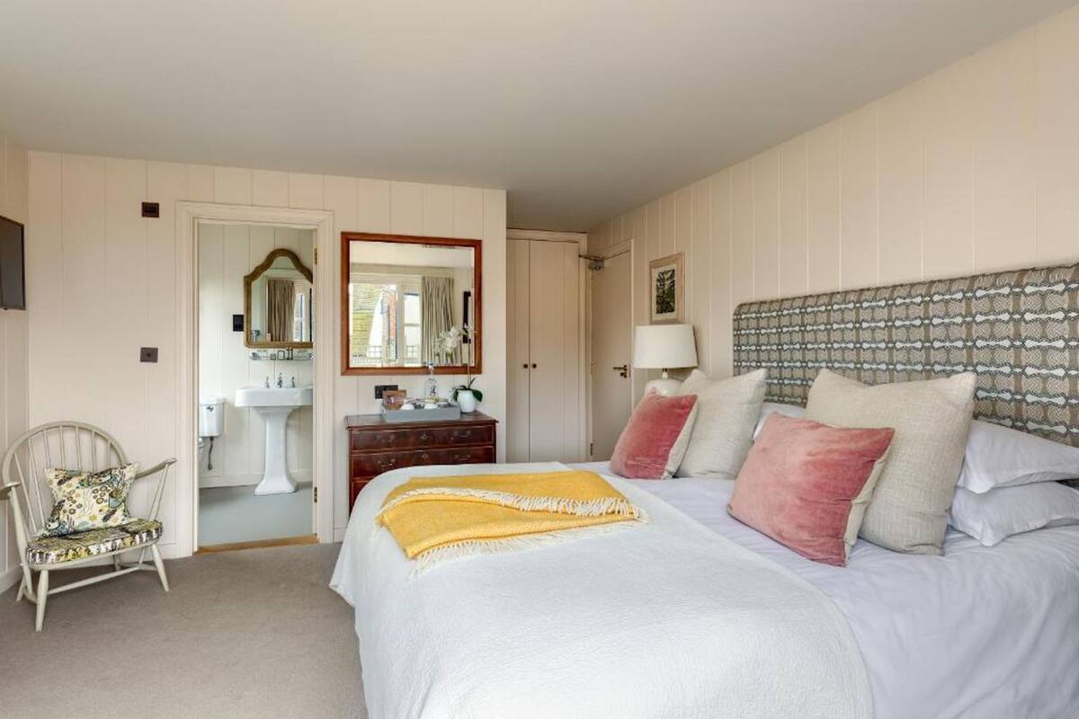 A bedroom with a large bed, a bedside table, a chair, a dresser, a mirror, and a window.