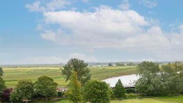 Vista de un paisaje rural con un extenso campo abierto, una zona cercada y una masa de agua al fondo.