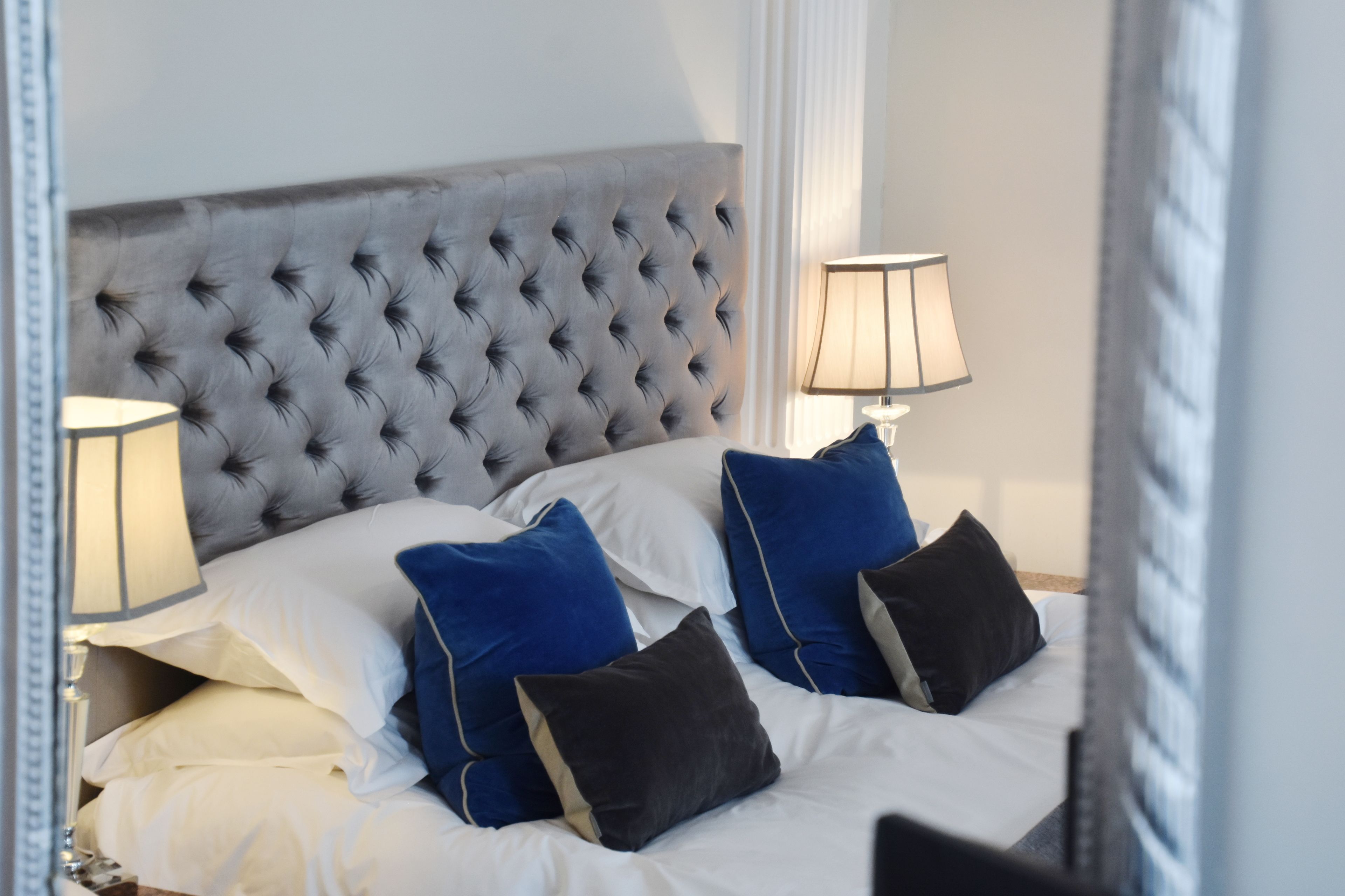 A neatly made bed with a tufted headboard, white and blue pillows, and two bedside lamps.