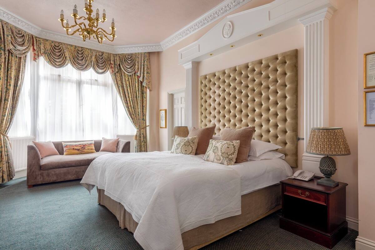 A hotel room with a large bed, a sofa, a nightstand, and a chandelier.