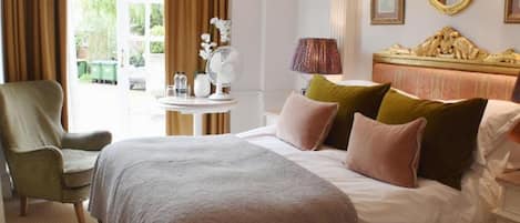 Habitación de hotel con una cama grande, una silla, una mesa con lámpara y una ventana con cortinas.