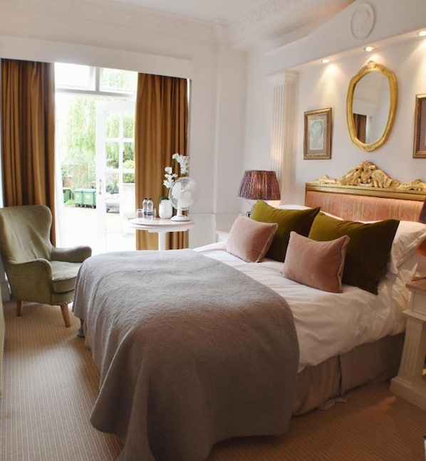 A hotel room with a large bed, a chair, a table with a lamp, and a window with curtains.