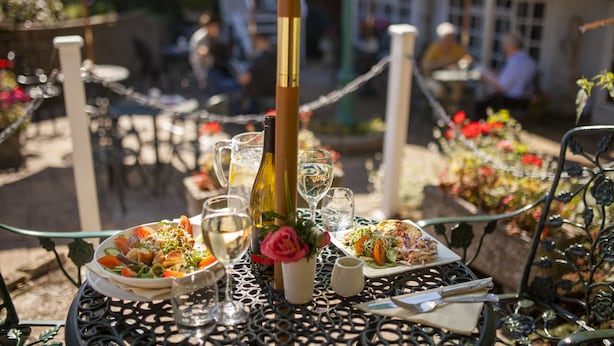 An outdoor dining area with tables set for meals, surrounded by greenery and umbrellas. - The Lookout Rye (Rye)