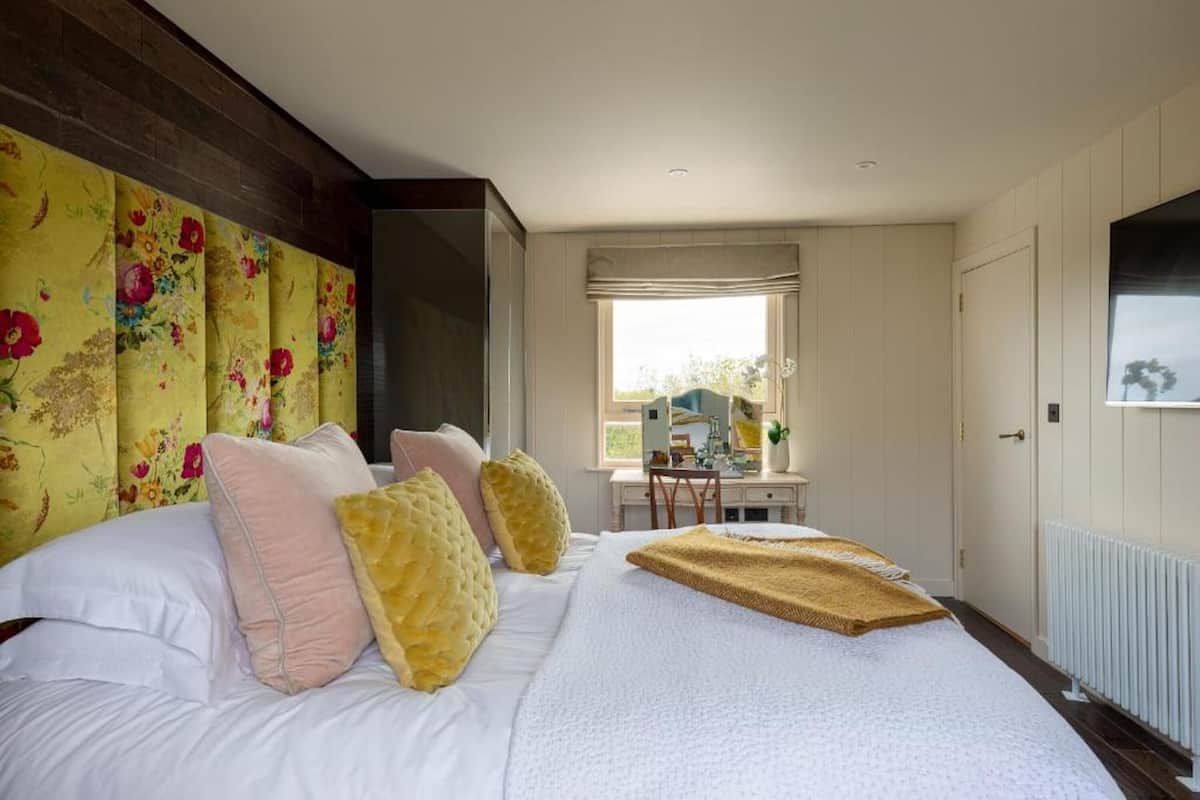 A bedroom with a large bed, a wooden headboard, a desk with a chair, and a window with a view.