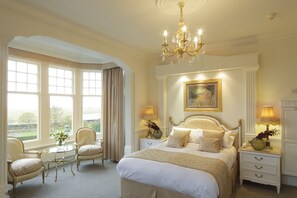 A spacious bedroom with a large bed, two bedside tables, a chandelier, and a view of the outdoors through large windows.