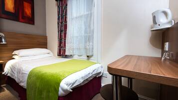 A hotel room with a bed, a desk, a chair, a window with curtains, and a wall-mounted coffee maker.