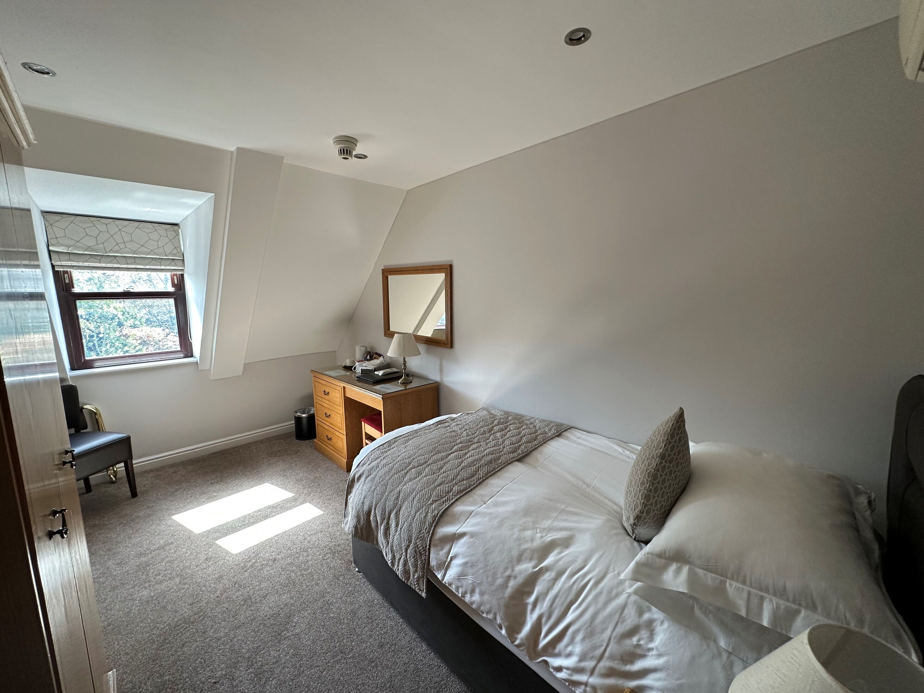 Een slaapkamer met een bed, een dressoir, een bureau, een raam en een spiegel.