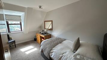 Een slaapkamer met een bed, een dressoir, een bureau, een raam en een spiegel.