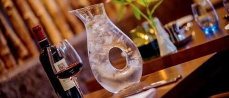 Una mesa de comedor con una botella de vino, una jarra de vidrio transparente y un florero con flores.