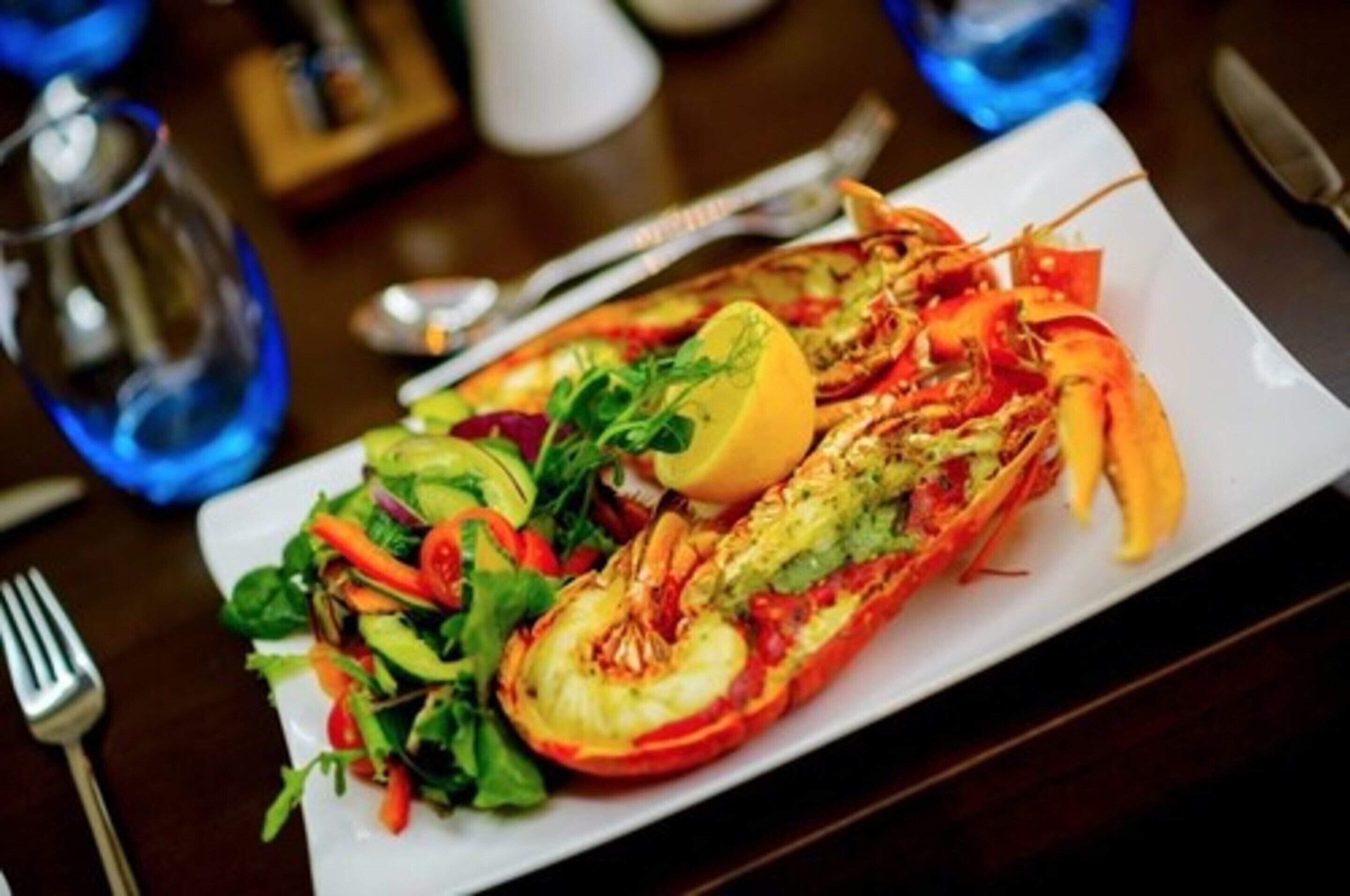 A lobster dish with a lemon wedge and a side salad on a white plate.