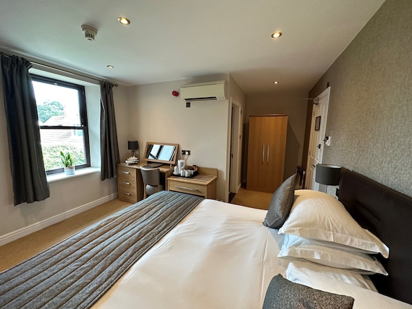 Une chambre d’hôtel avec un grand lit, un bureau avec un ordinateur, une chaise, une armoire et une fenêtre avec des rideaux.