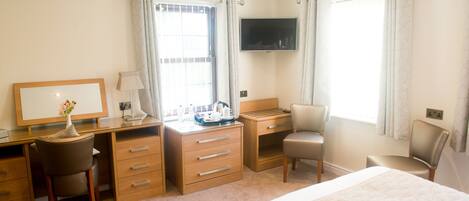 A hotel room with a bed, a desk with a chair, a TV mounted on the wall, and a window with curtains.