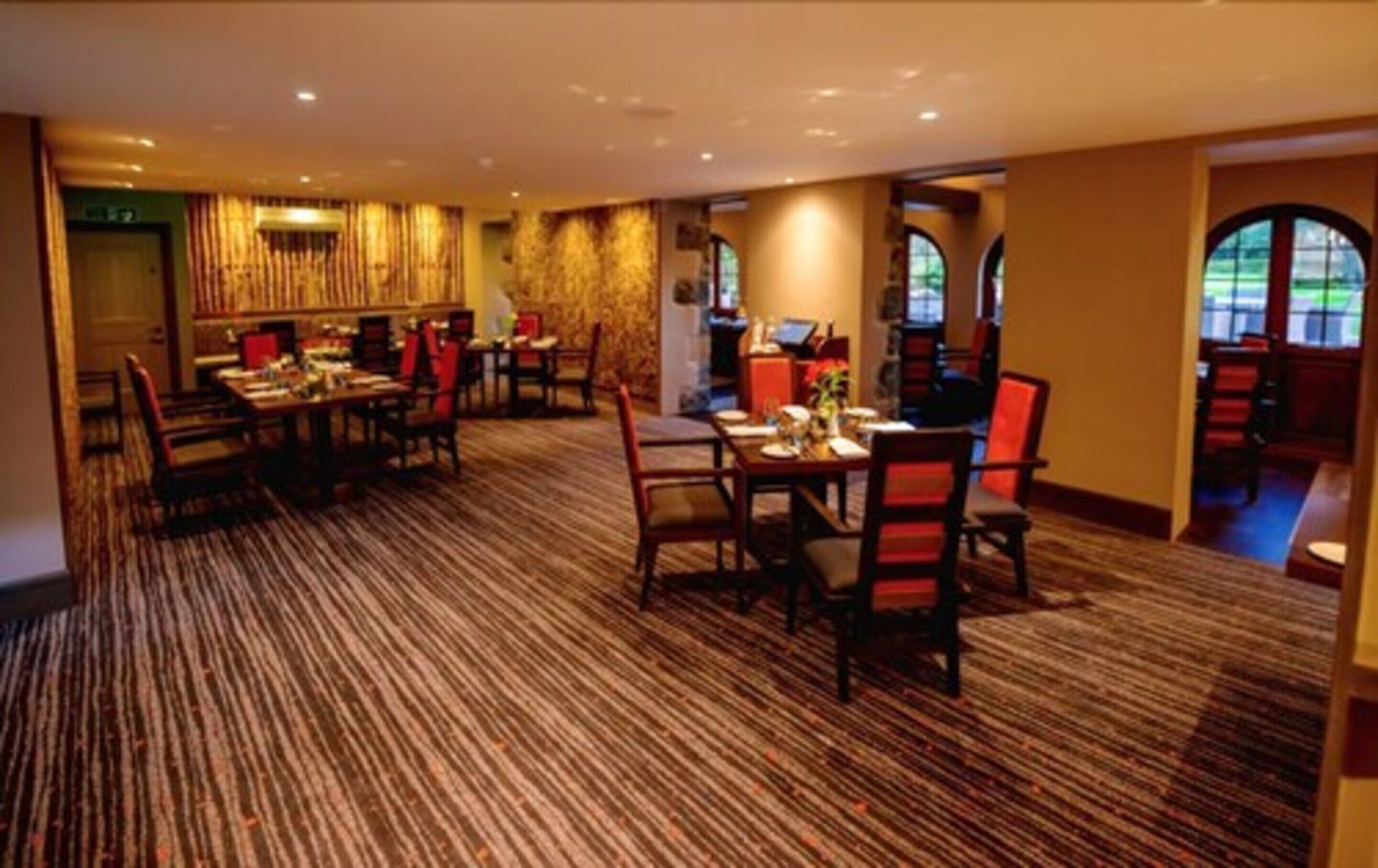 Zona de dinar d'hotel amb diverses taules i cadires, sòls amb moqueta i una zona de bar amb una paret de pedra.
