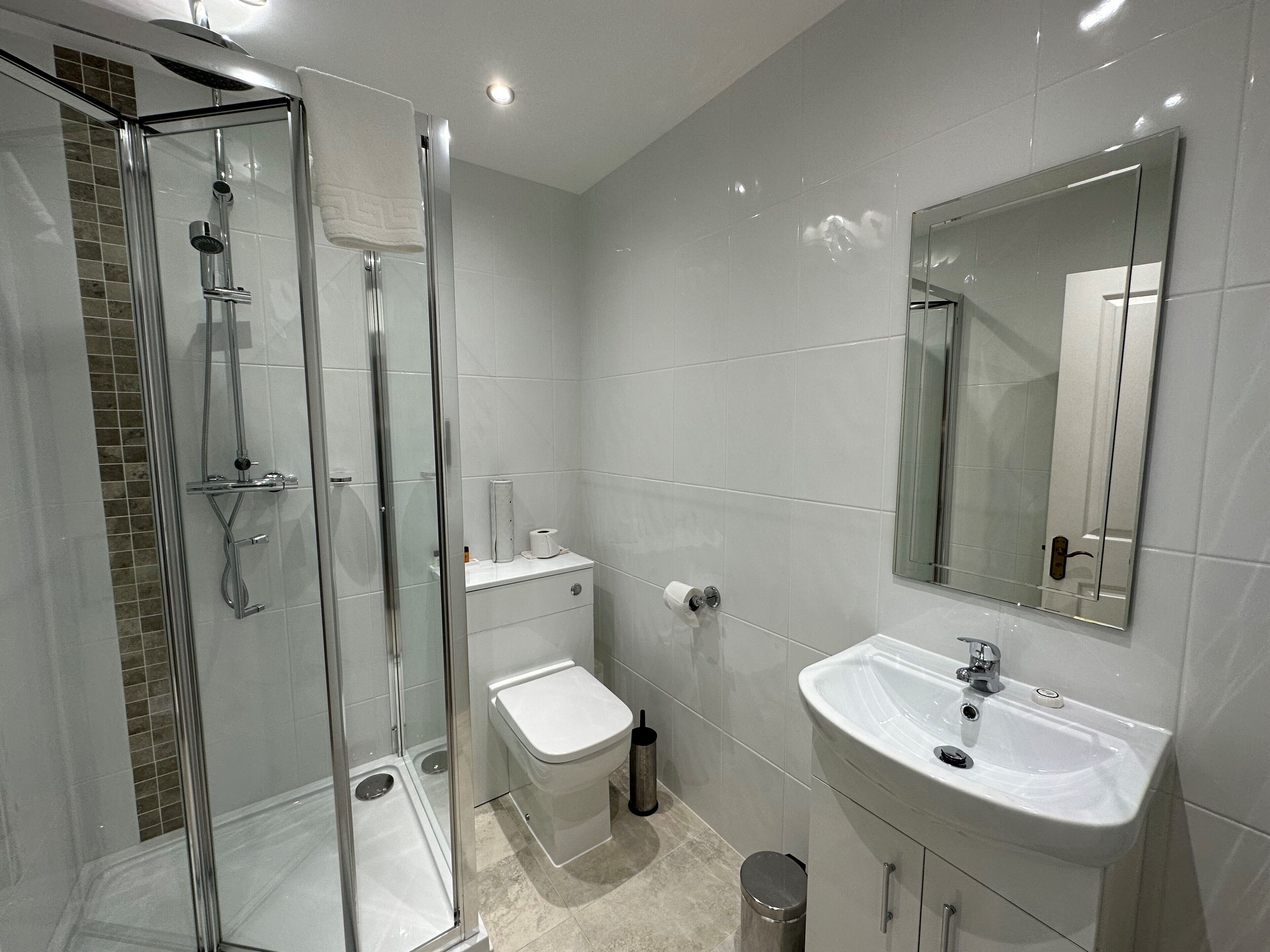 A modern bathroom with a glass-enclosed shower, a white toilet, a sink with a mirror, and tiled walls.