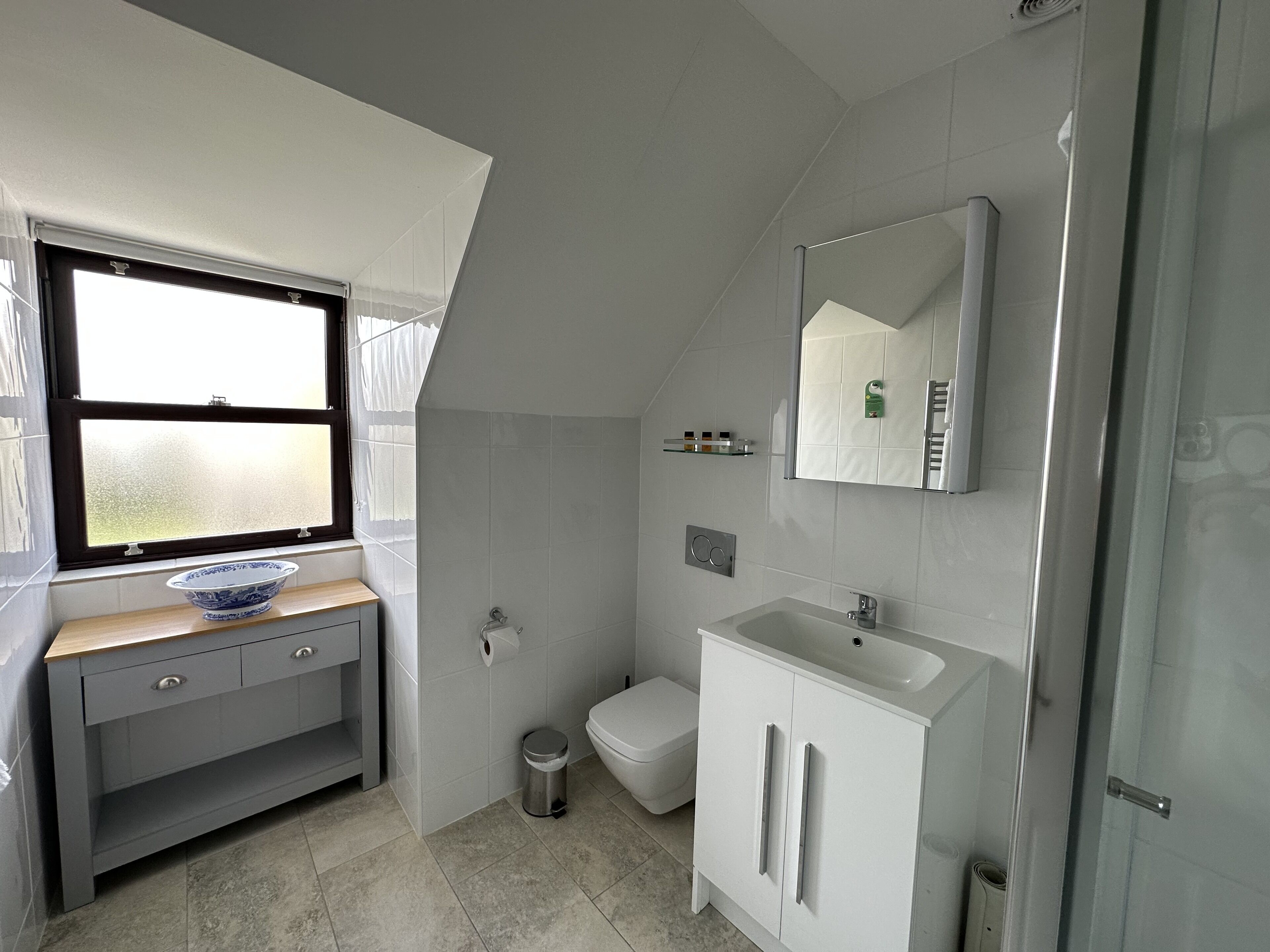 Un baño moderno con ventana, lavamanos, inodoro y espejo.