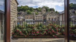 A stone building with a clock tower, surrounded by other stone buildings and greenery. - The Old Bridge Inn, Holmfirth, West Yorkshire (Holmfirth)