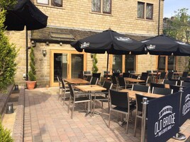 An outdoor patio area with tables and chairs, covered by umbrellas, and a sign reading "Old Bridge Inn & Coffee House".