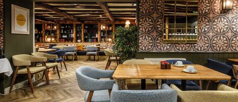 A cozy restaurant interior with wooden floors, patterned wallpaper, and a variety of seating options including tables and chairs.