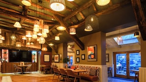 A spacious interior with high ceilings, exposed wooden beams, and multiple hanging pendant lights. There is a seating area with a sofa and chairs, a dining table, and a television mounted on the wall. - The Old Bridge Inn, Holmfirth, West Yorkshire (Holmfirth)