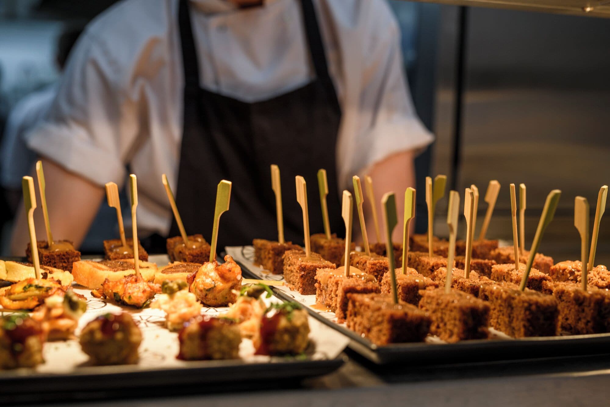 A variety of appetizers arranged on trays, including bread cubes and meatballs, with toothpicks inserted.