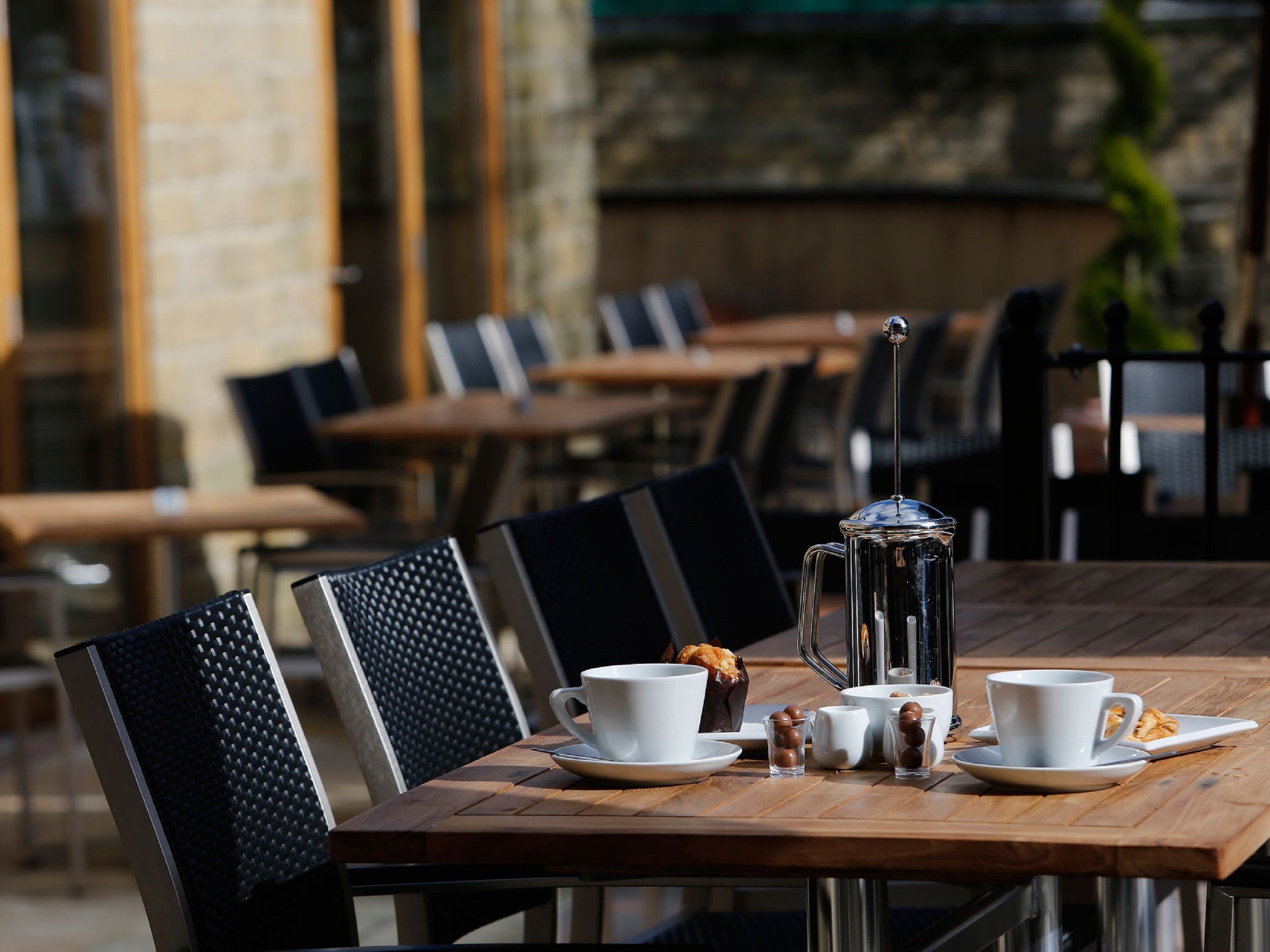 A café table set with white cups, saucers, a coffee pot, and small glass cups with round objects.