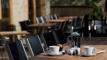A café table set with white cups, saucers, a coffee pot, and small glass cups with round objects.