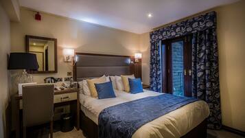 Habitación de hotel con cama, escritorio, silla y ventana con cortinas.
