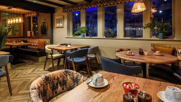 A cozy restaurant with wooden tables and chairs, large windows with city views, and hanging wicker lamps.