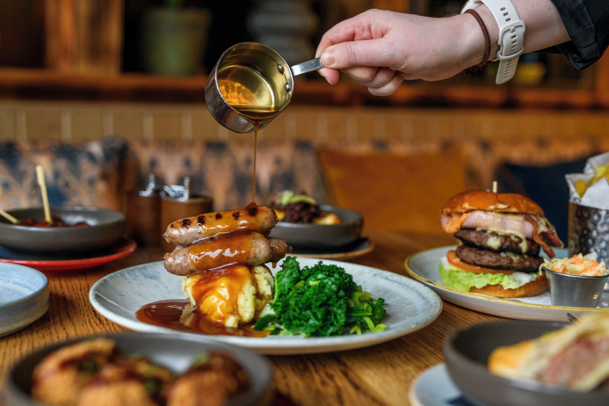 A dining table with various dishes including sausages, a burger, and a salad.