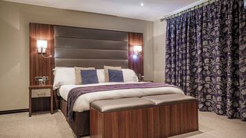 Un dormitorio de hotel moderno con una cama grande, cabecera de madera, lámparas de noche y cortina floral oscura.