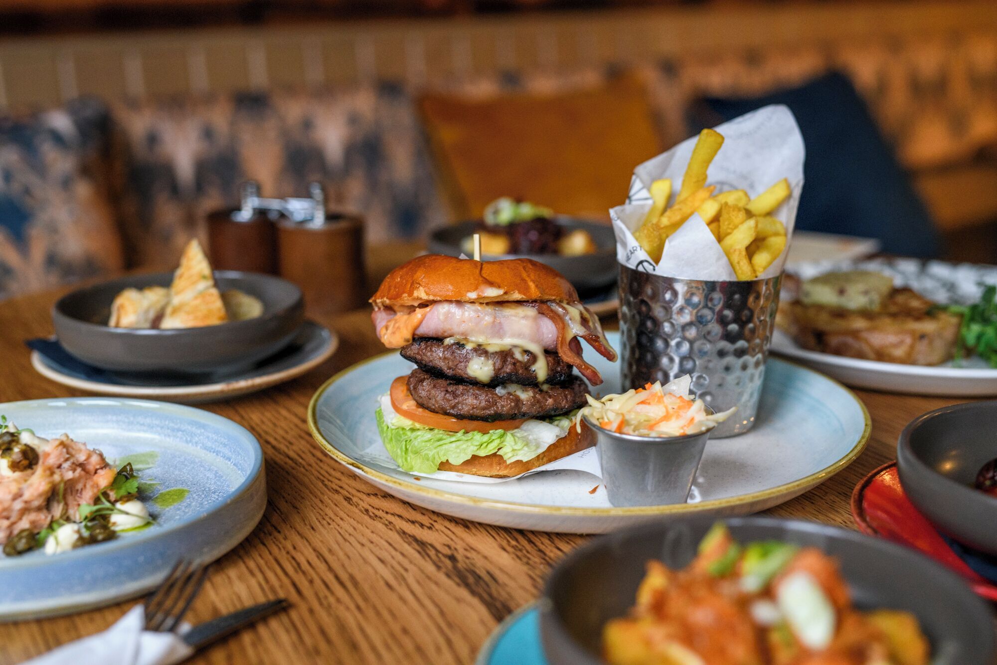 Una mesa de comedor con diversos platos, incluyendo una hamburguesa, papas fritas y una ensalada.