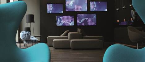 A modern living room with a sectional sofa, teal armchairs, and multiple screens displaying abstract patterns.