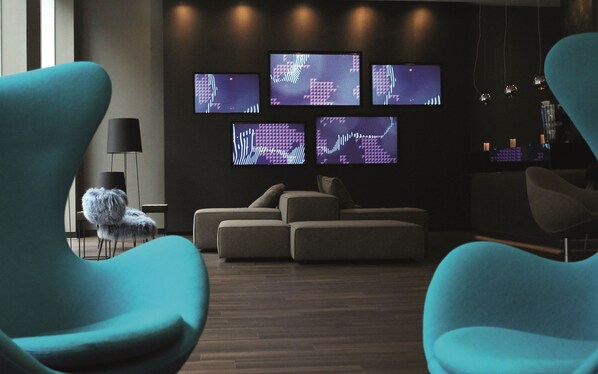 A modern living room with a sectional sofa, teal armchairs, and multiple screens displaying abstract patterns.