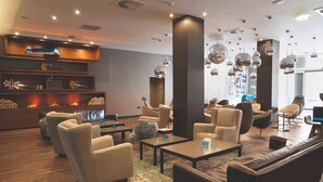 Un espace de détente moderne, avec des canapés, des fauteuils et une table basse. On y trouve des étagères ornées d’objets décoratifs et une cheminée.