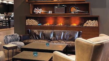 A modern lounge area with leather sofas, a coffee table, and a fireplace with logs.