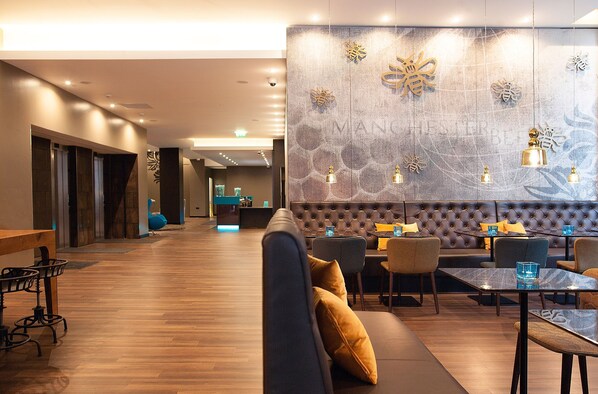 Un hall d’hôtel moderne comprenant un espace salon, un comptoir d’accueil et un mur agrémenté d’éléments décoratifs.
