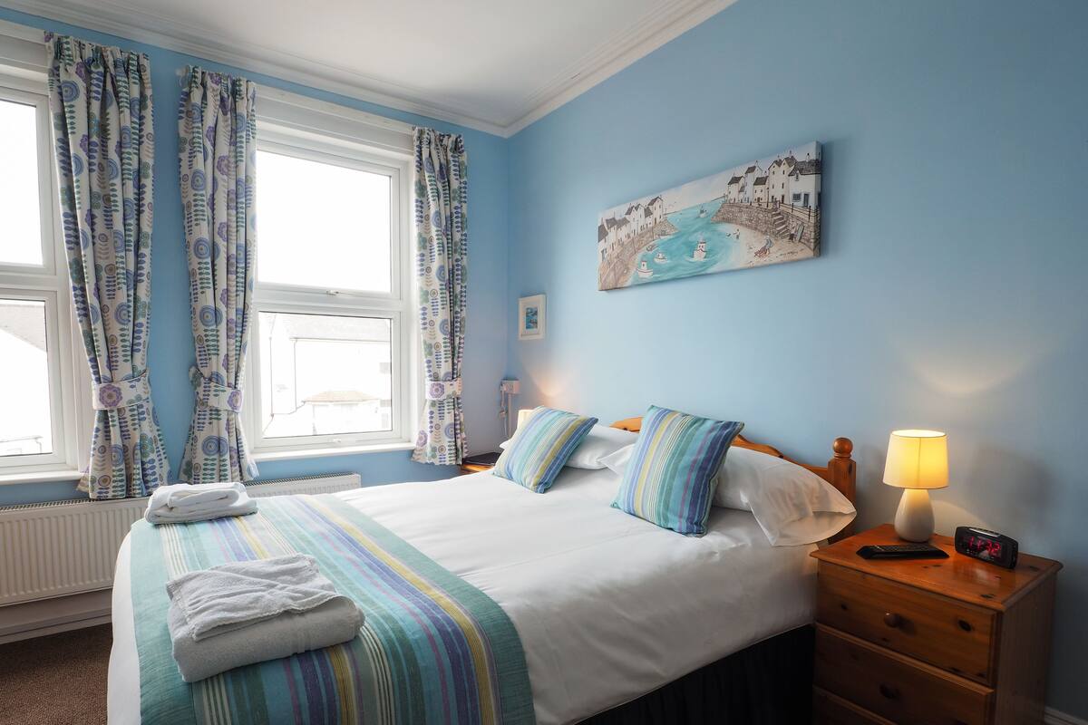 A bedroom with a bed, a nightstand, a lamp, a painting, and curtains.