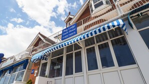 Ein Hotel mit einer blau-weiß gestreiften Markise, einem Schild mit der Aufschrift 'Bay Lodge Guest House' und einem Schild mit der Aufschrift 'Freie Zimmer' im Fenster.