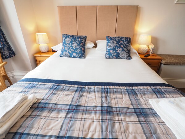 A neatly made bed with a blue and white checkered bedspread, two matching blue floral pillows, and a wooden headboard.