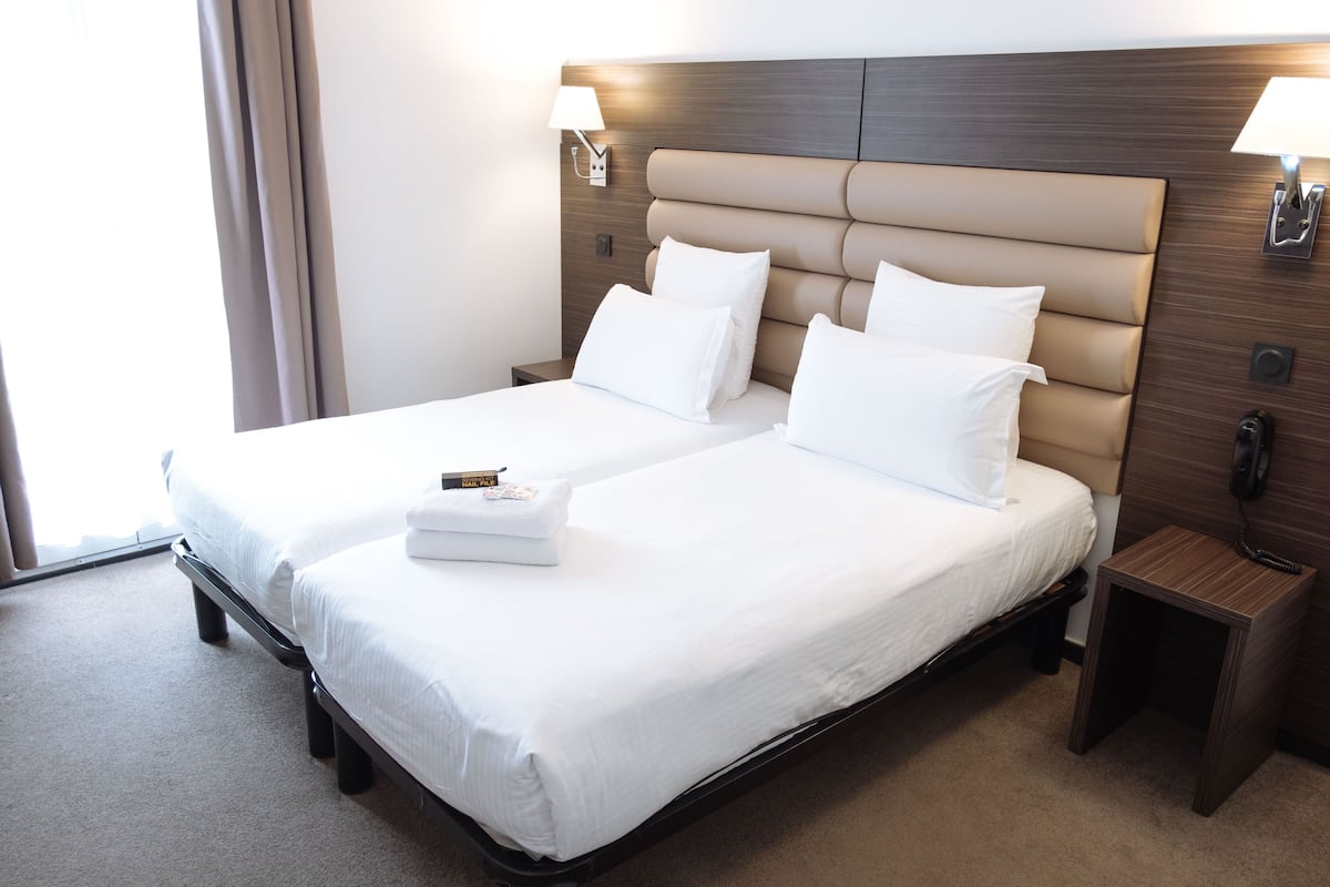 A hotel room with a large bed, two bedside tables, a nightstand, and a lamp on each side of the bed.