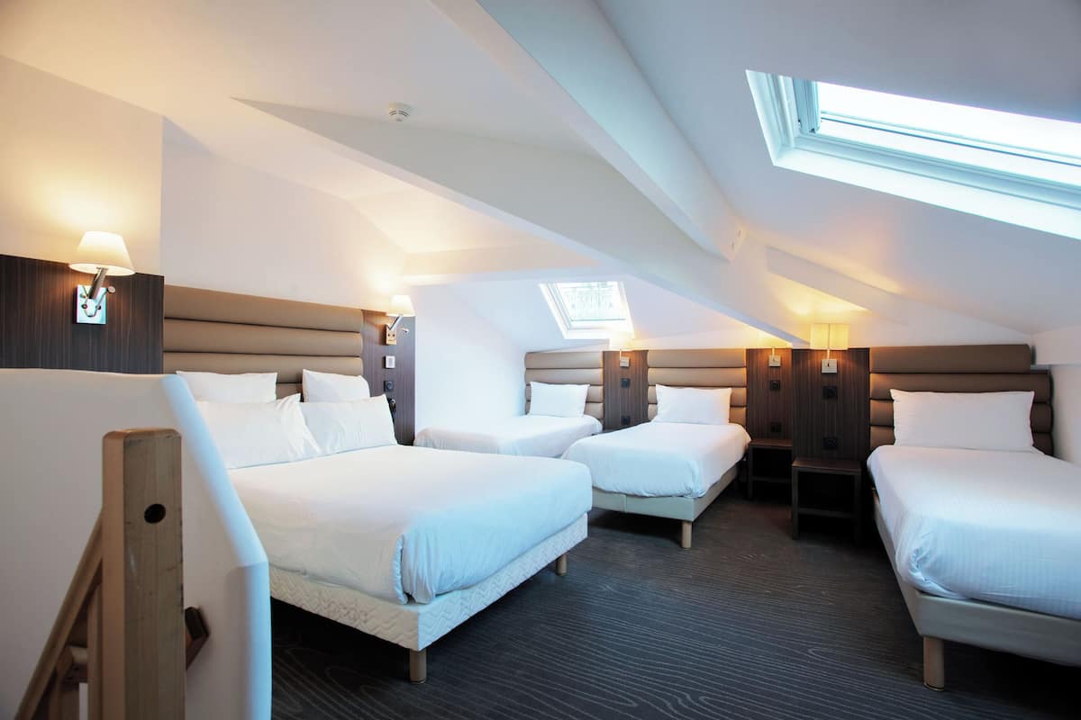 A hotel room with three beds arranged in a row, a skylight, and a wooden headboard.