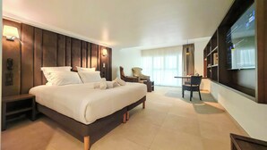 A hotel room with a large bed, a desk, a chair, a TV, and a window with curtains. - Hôtel & Appartements Monsigny (Nice)