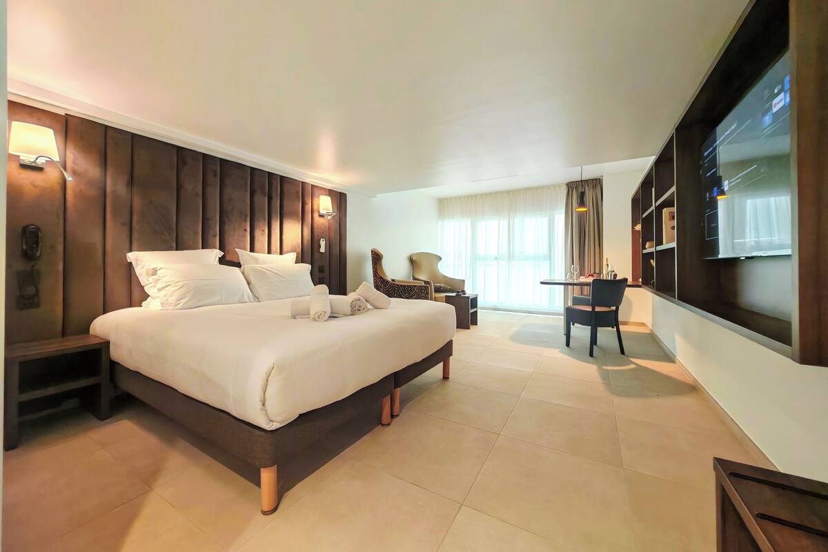 A hotel room with a large bed, a desk, a chair, a TV, and a window with curtains.