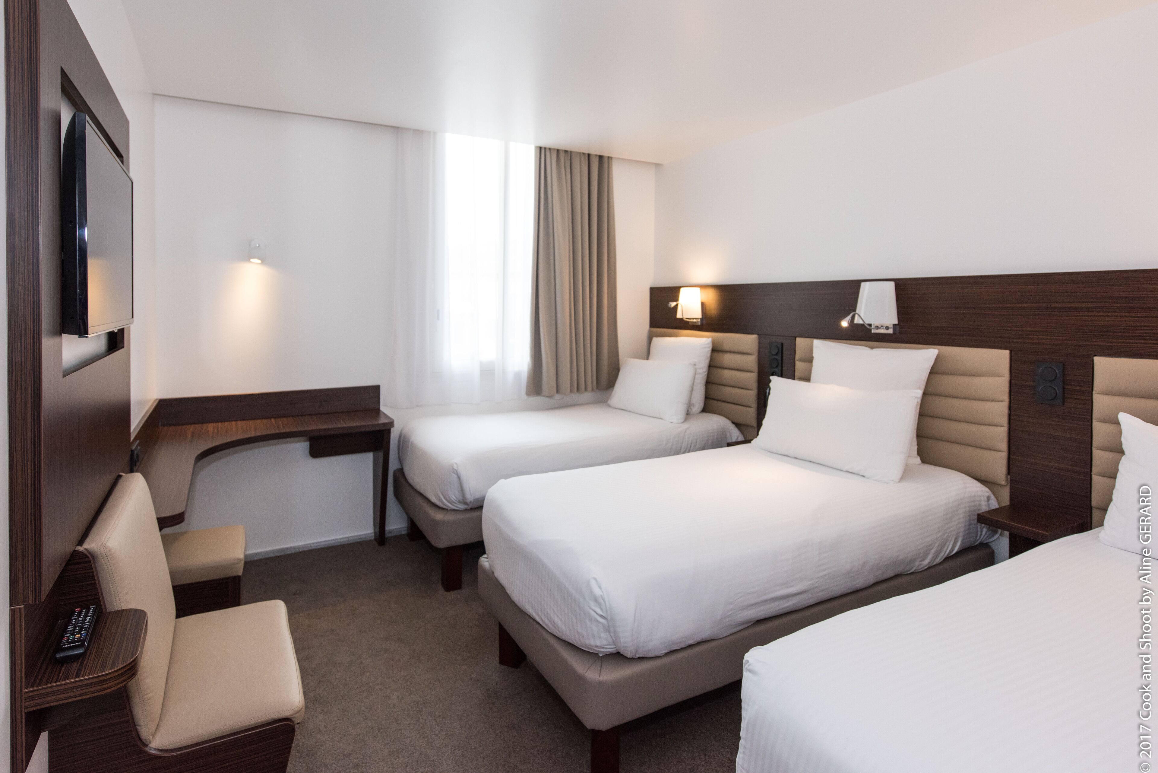 A hotel room with two beds, a desk, a chair, and a TV.