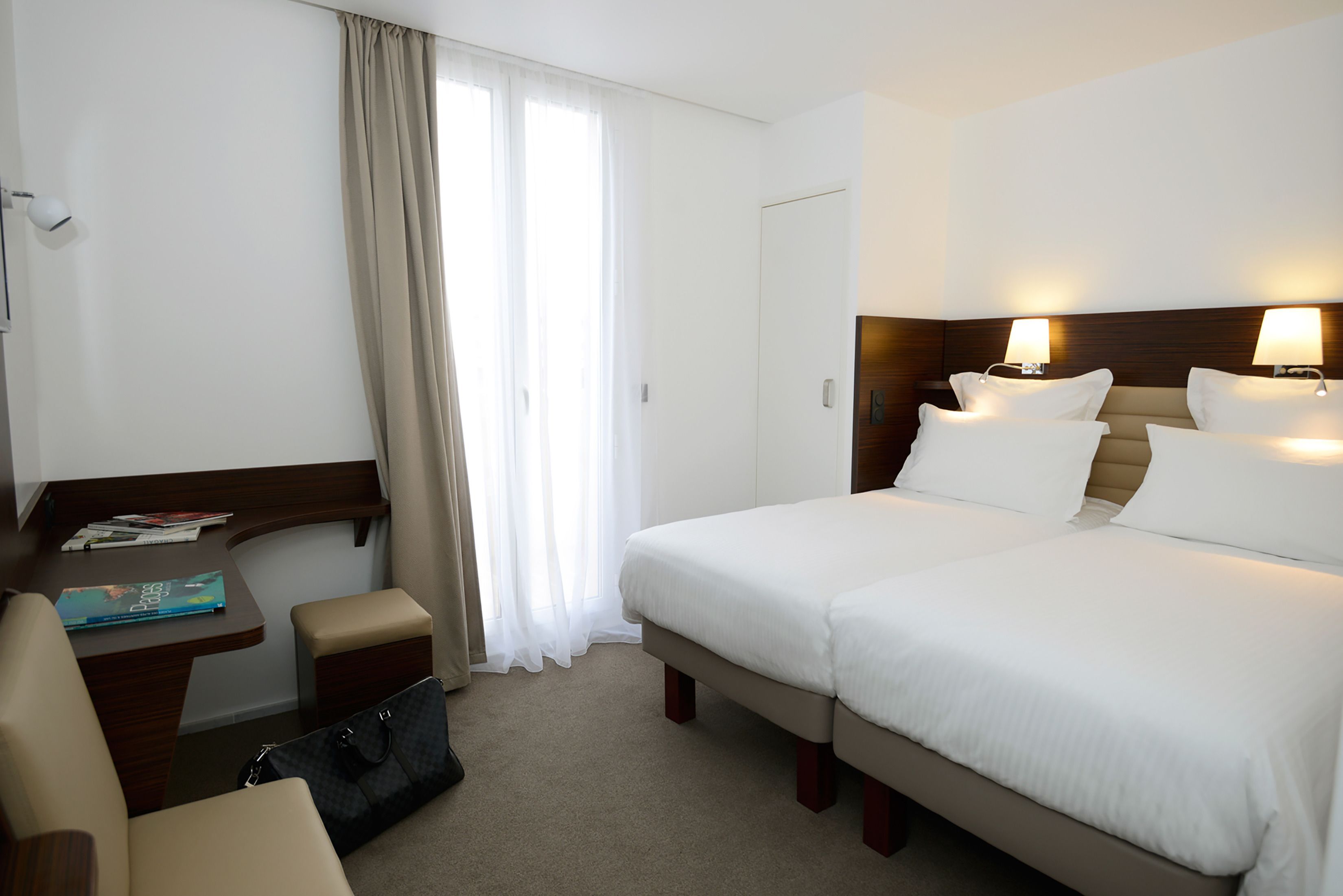 A hotel room with a bed, bedside tables, a desk, a chair, and a window with curtains.