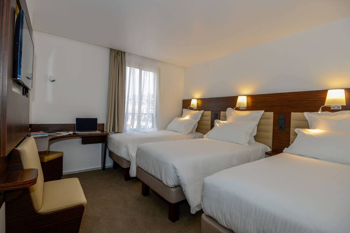 A hotel room with two beds, a desk, a chair, and a TV.